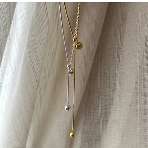Detail of silver and gold Y-shaped necklaces with ball pendants on soft white fabric
