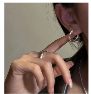 Close-up of silver woven texture ring and earrings with gold accent on person