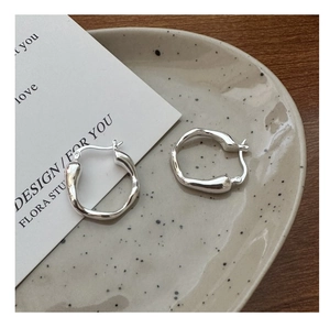 Detail of minimalist liquid silver earrings on a ceramic tray with a warm wood background