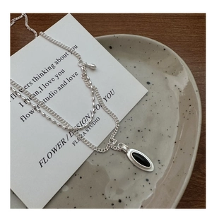 Macro detail of silver double-layered necklace with black oval pendant on ceramic plate