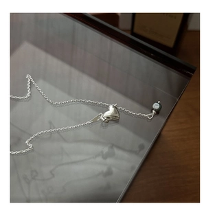Detail of silver heart pendant necklace with elegant dark pearl accent on a glass tray