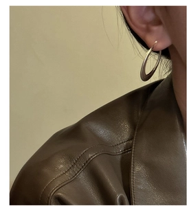 Gros plan d'une grande créole argentée mate sur mannequin avec cuir marron minimaliste