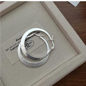Gros plan de créoles en argent sterling S925 avec une texture au fini mat brossé