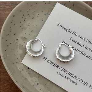Macro detail of matte S925 sterling silver hoop earrings with wavy texture on ceramic dish
