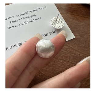 Close-up of S925 sterling silver stud earrings with brushed texture and grid back