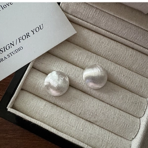 Detailed macro view of silver brushed metal stud earrings in a minimalist dome design