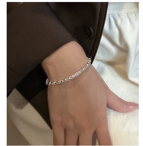 Close-up of minimalist silver bamboo link bracelet worn with a professional brown suit
