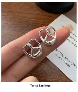 Close-up of S925 sterling silver pretzel knot stud earrings held by hand over a desk