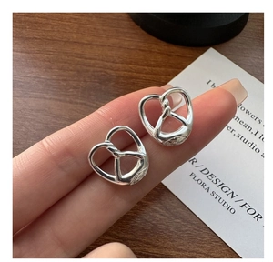 Close-up of S925 sterling silver pretzel heart stud earrings on a minimalist wooden surface