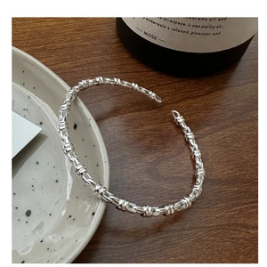 Macro view of silver twisted knot open cuff bracelet on a minimalist ceramic plate