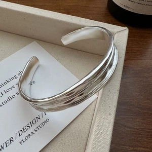 Minimalist S925 sterling silver open bangle with organic wavy texture on a fabric tray