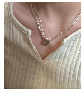 Dettaglio macro della collana a tre strati in argento con pendente a cubo martellato