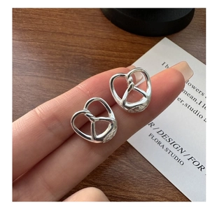 Detail of S925 silver pretzel heart studs with a polished mirror finish on wood