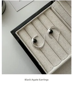 Close-up of S925 silver C-shaped earrings with black agate beads in a beige velvet box