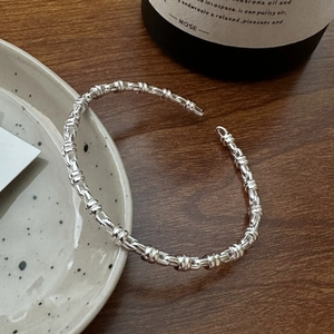 Polished S925 sterling silver open bangle with a twisted link design on a ceramic plate