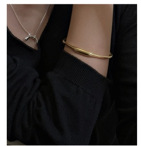 Dettaglio di un bracciale rigido dorato e una collana argentata su tessuto nero a maglia