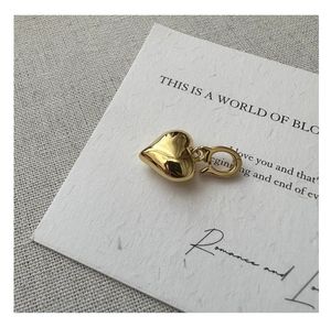 Macro detail of glossy golden heart pendant with metallic clasp on textured paper