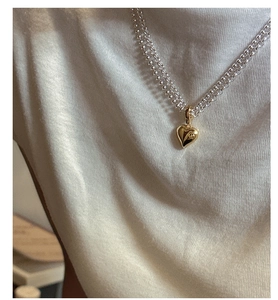 Detail of layered gold heart pendant necklace on minimalist beaded and cable chains