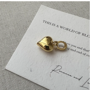 Close-up of heart-shaped pendant in polished gold finish with a spring clasp hook