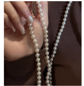 Detail of hand holding long white pearl necklace against a vintage brown sweater