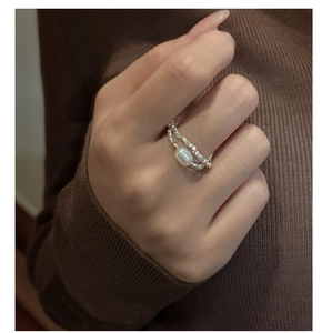 Dettaglio di un anello con perla e sfere metalliche sulla mano con maglione autunnale