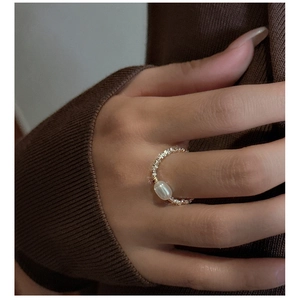 Dettaglio dell'anello in argento S925 con perla indossato su uno sfondo in maglia marrone