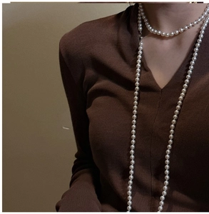 Detail of layered S925 silver pearl long necklace worn over a brown V-neck sweater
