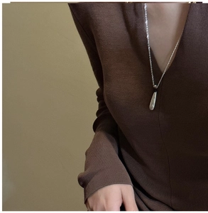 Close-up of a silver teardrop pendant necklace worn over a dark brown knit sweater