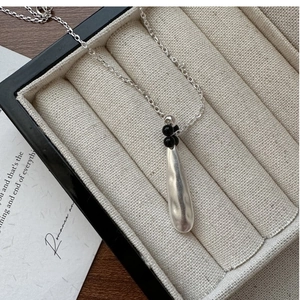Macro detail of silver teardrop pendant with black beads in a velvet jewelry box