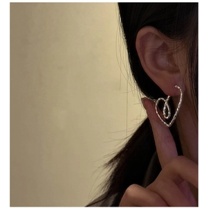 Detail view of heart-shaped silver earrings with textured finish on model ear