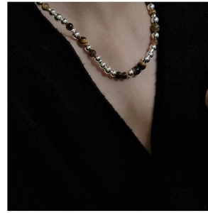 Détail de perles d'argent et collier œil de tigre brun porté sur un col roulé noir