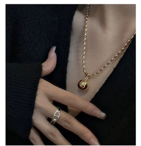 Detailed view of a gold spherical pendant necklace and silver chain link ring on a model