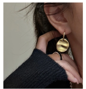Detail of gold-plated earrings featuring irregular disc shape and hammered texture design