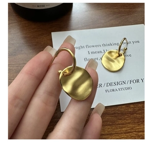 Detailed macro of matte gold earrings featuring unique wavy texture on irregular discs