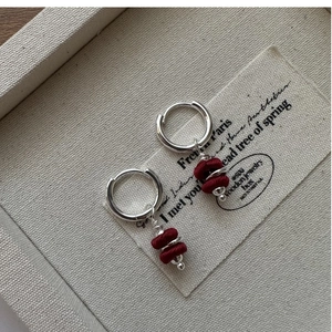 Macro detail of S925 silver hoop earrings with red thread wrapped charms and metal beads