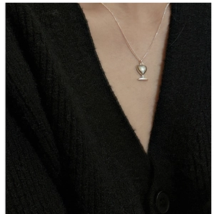 Gros plan d'un collier pendentif calice en argent S925 porté sur un tricot noir
