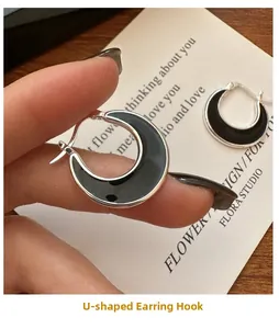 Close-up of U-shaped silver hoop earrings with black enamel detail on a minimalist card