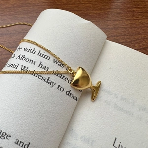 Collier avec pendentif gobelet doré sur une page de livre, chaîne fine minimaliste