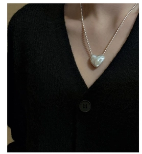 Detail of silver heart pendant with hammered texture worn on a model with black cardigan
