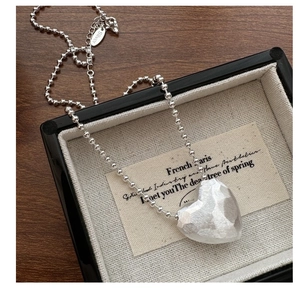 Macro detail of S925 silver heart pendant with hammered texture and beaded chain in a tray