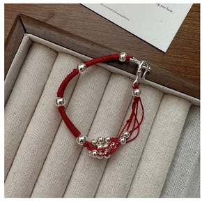 Detailed view of handmade red string bracelet with silver beads on velvet tray