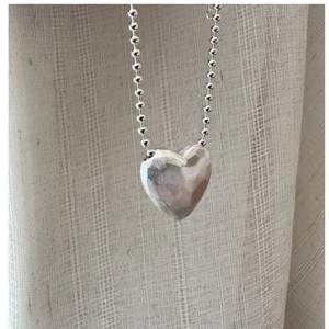 Macro detail of textured sterling silver heart pendant on a stylish bead chain necklace