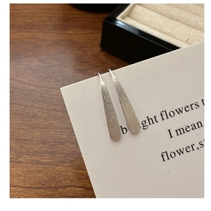 Macro shot of brushed S925 sterling silver drop earrings on a white display card