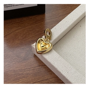 Gros plan d'un pendentif cœur doré minimaliste posé sur un support en tissu blanc