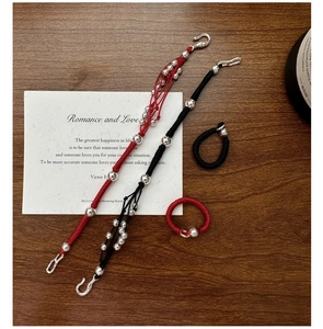 Close-up of red and black woven cords with silver beads on a dark wood background