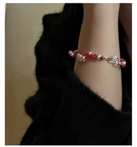 Detail view of a woven red string bracelet with silver beads and S-hook clasp closure