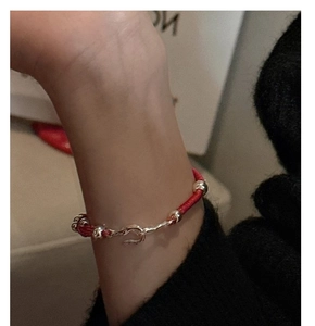 Close-up of a red woven rope bracelet with irregular silver clasp and beads on wrist