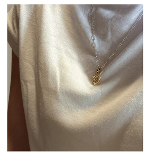Détail d'un collier pendentif cœur doré sur chaîne trombone porté par un mannequin femme
