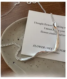 Macro shot of minimalist silver wavy pendant and Cuban link chain on a ceramic plate