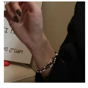 Detail of layered black cord bracelet with silver beads on a model's wrist